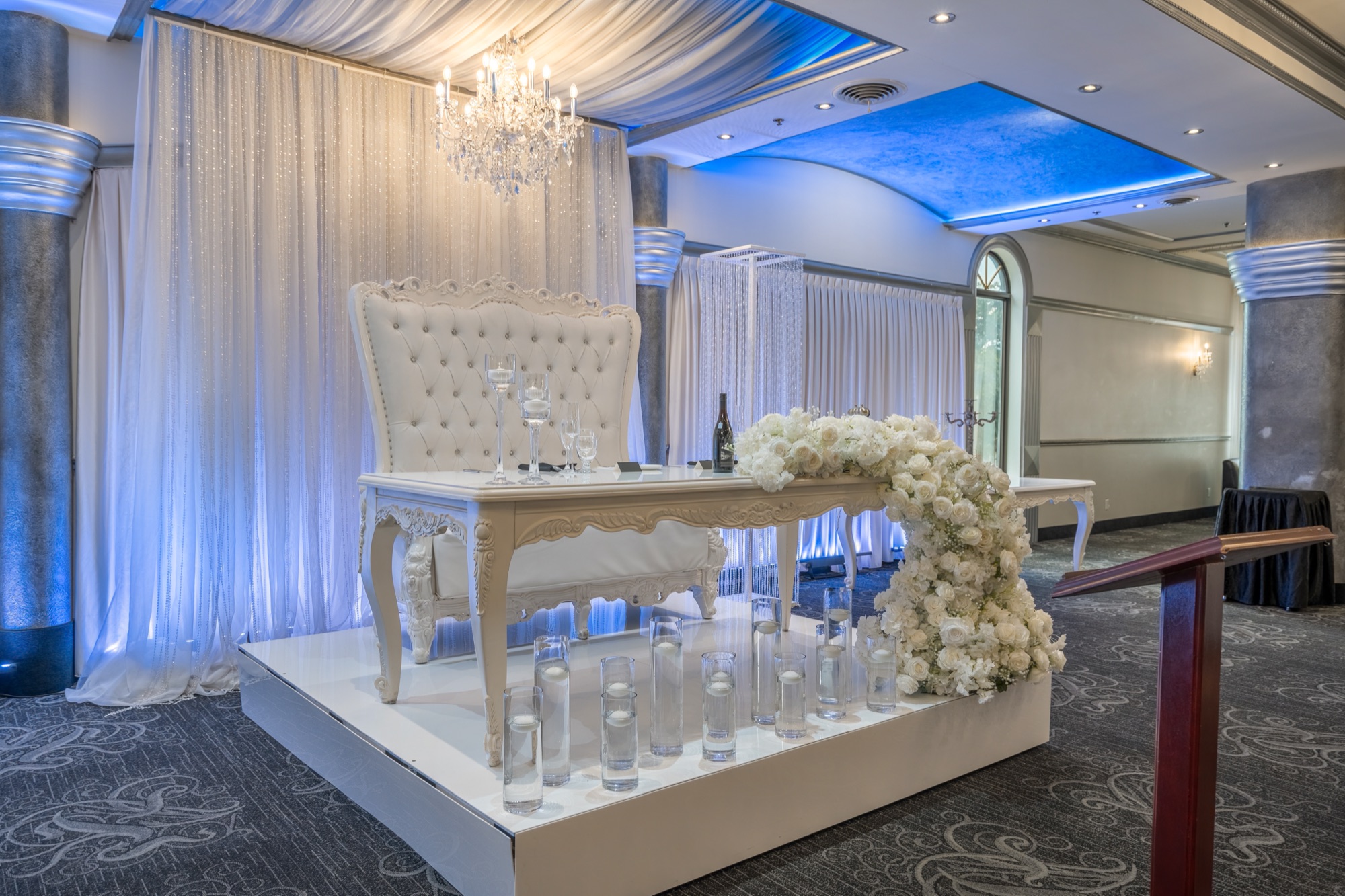 Sweetheart table beneath drapery and chandeliers